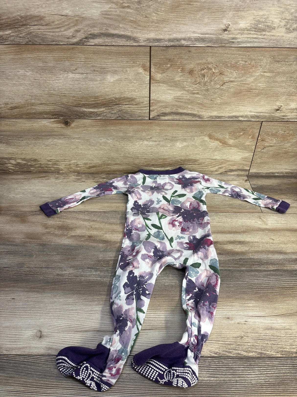 Back view of Burt's Bees Baby floral footed sleeper showcasing purple watercolor floral print, long sleeves, and purple non slip soles on wood floor