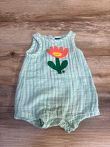 Green and white striped baby romper with a smiling flower graphic on wooden background