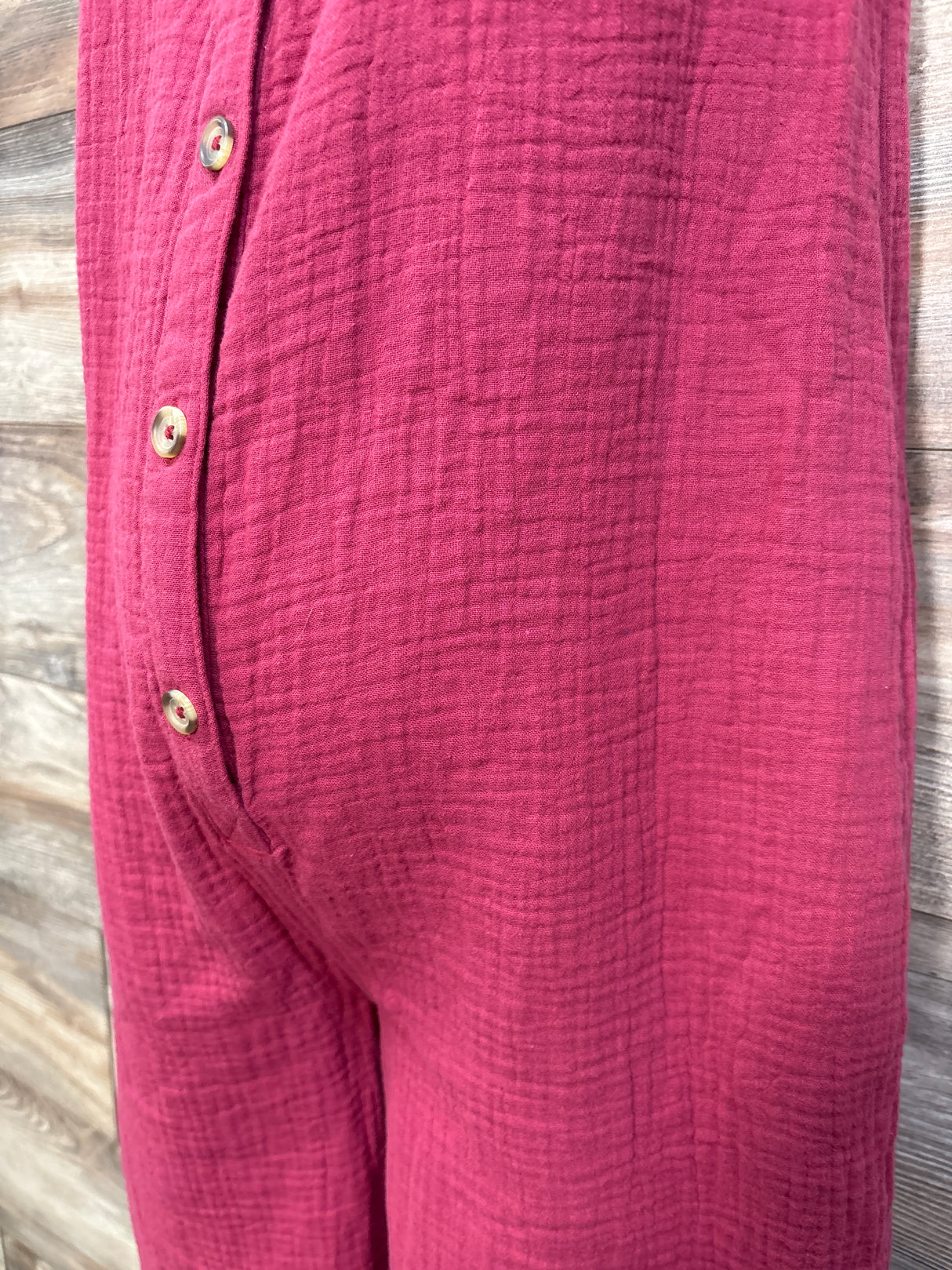 Close-up of Isabel maternity gauze jumpsuit showing front button placket and textured burgundy gauze fabric against wood background
