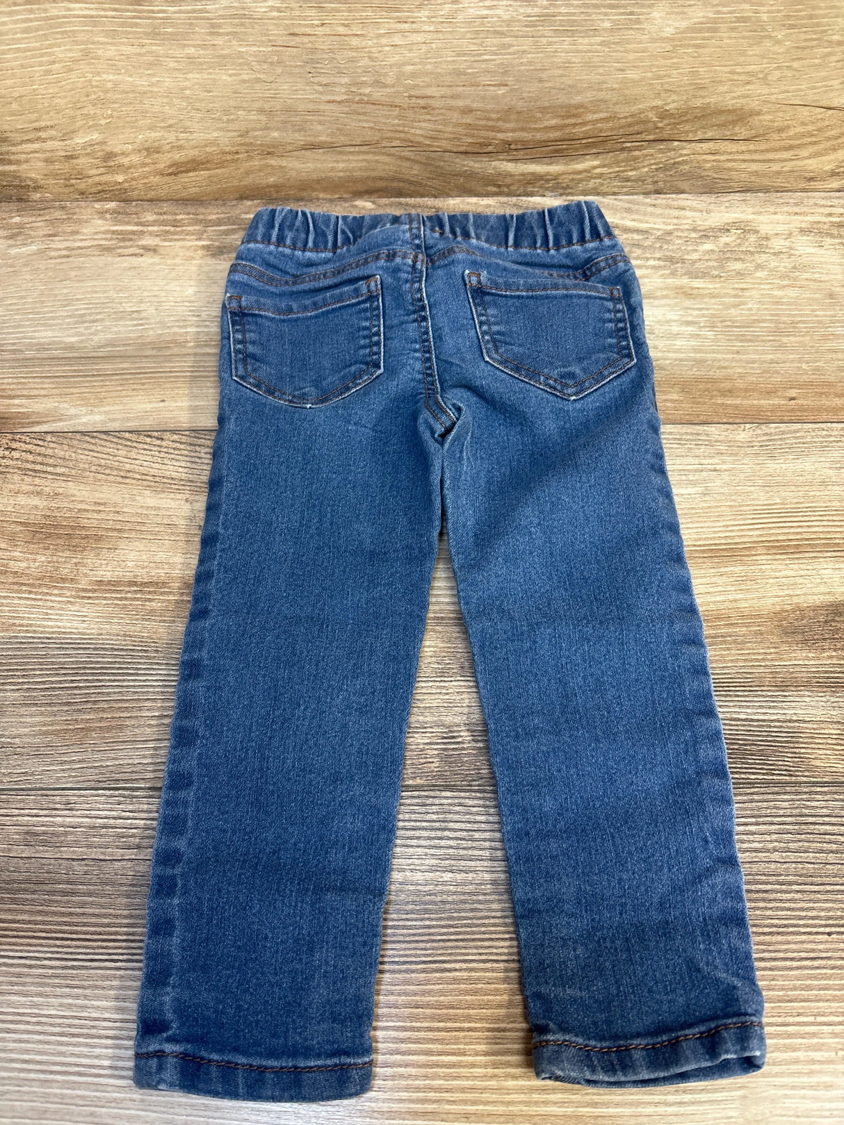 Back view of children's blue denim jeans with elastic waistband on wood background