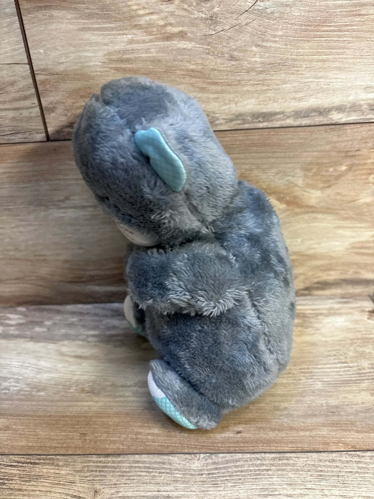 Gray plush elephant toy with blue ear and foot accents on wooden floor