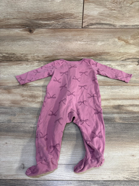 Flat-lay of back of purple footed baby sleeper showcasing all-over bow print on wooden background