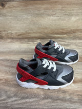 Angled side view of Nike Huarache TD sneakers size 8C showing red heel strap, white laces, gray upper and white sole on wood