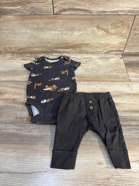 Baby boy outfit with dark tractor print onesie and black pants on wood floor