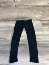 Flat-lay of toddler black leggings (size 2T) showing elastic waistband and slim tapered legs on light wood floor