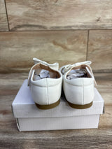 Rear view of white leather baby princess flats size 7C showcasing bows and tan rubber soles on a white shoebox and wood floor