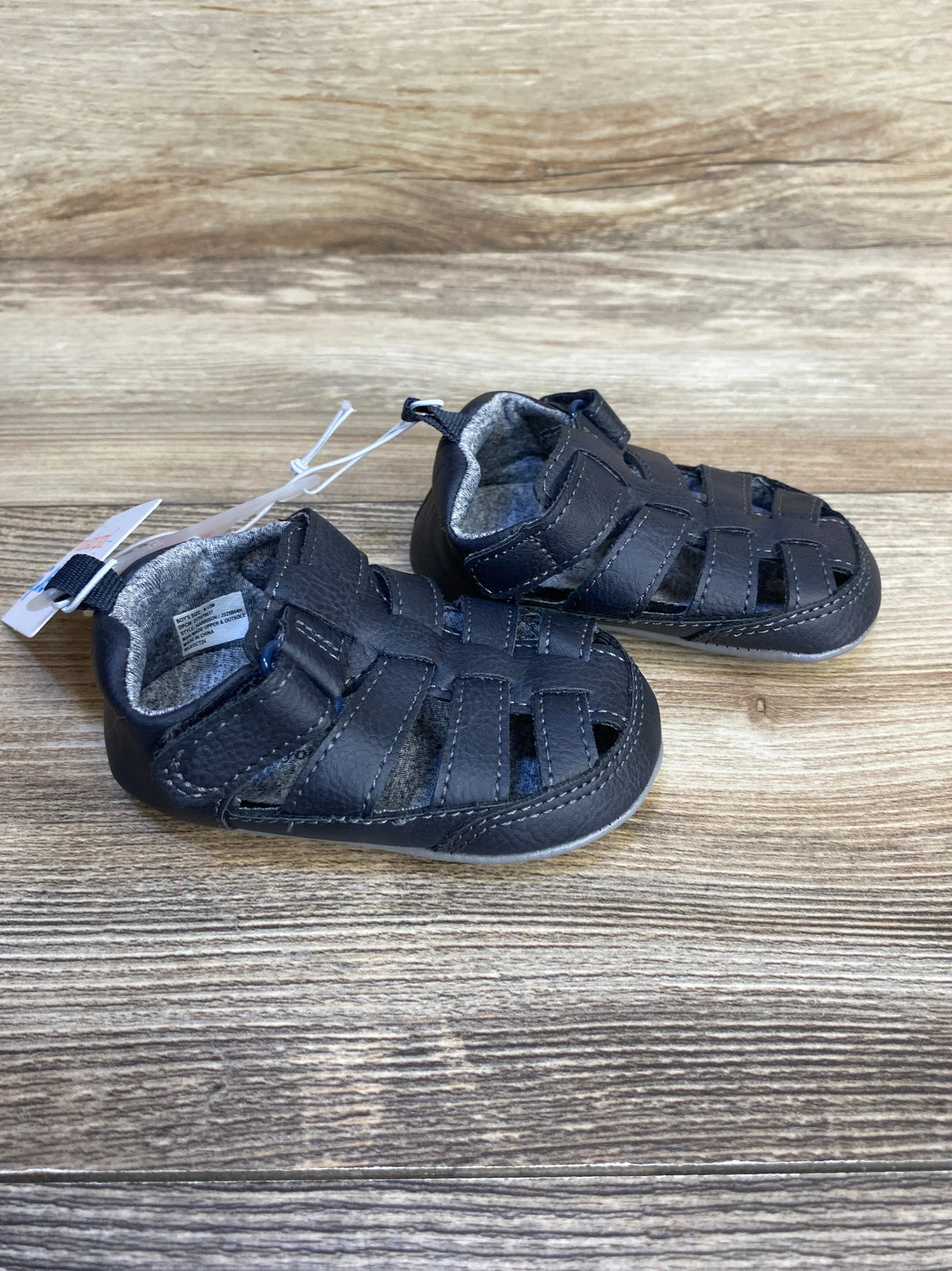 Three-quarter view of Just One You Harrison fisherman baby sandals in navy showcasing velcro strap closure and woven toe upper on wood surface