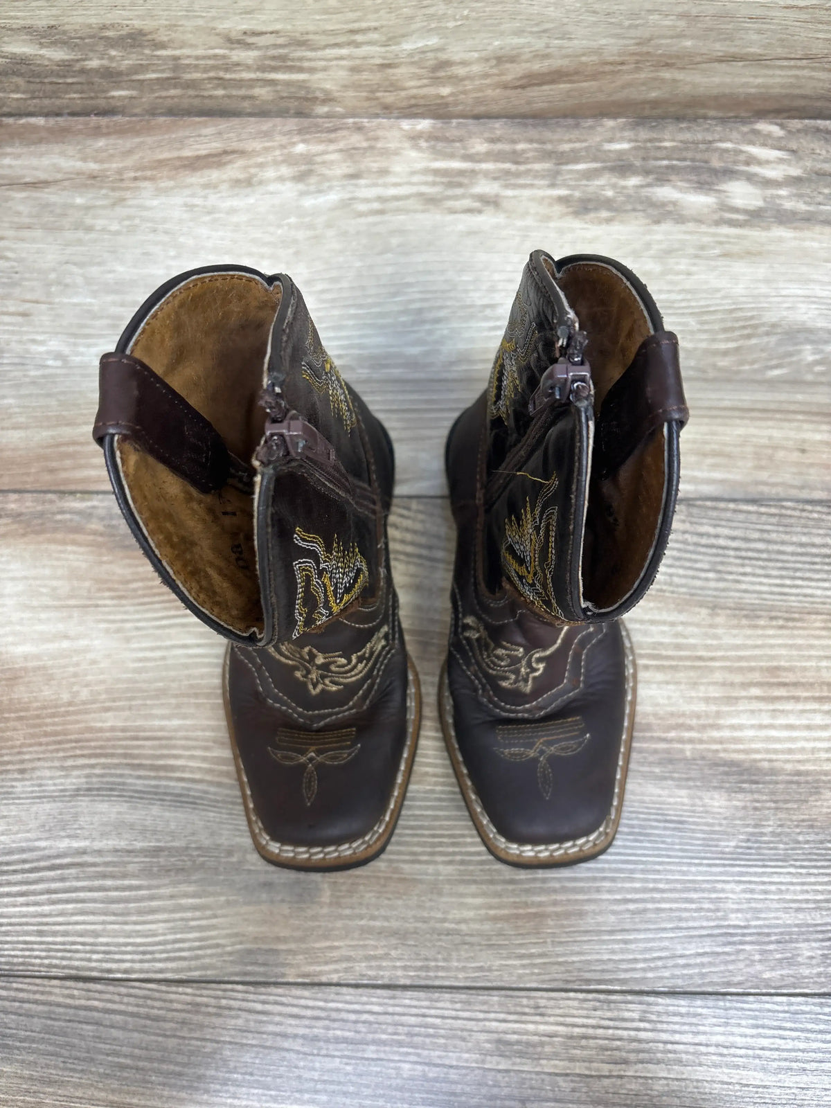 Top view of Texas Gold Minors brown square toe kids cowboy boots showcasing embroidered details and side zippers on a wood background