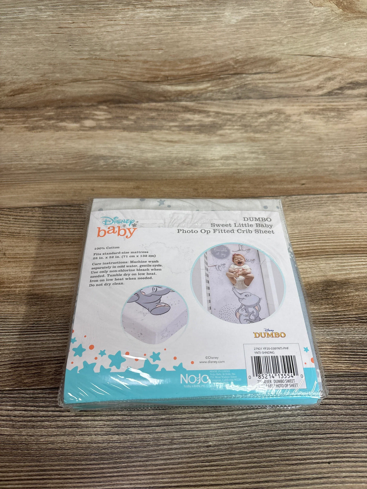 Top-down view of Disney Dumbo fitted crib sheet in packaging showcasing Dumbo photo-op print and brand on wood floor