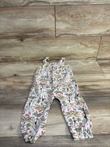 Flat lay of cream sleeveless toddler jumpsuit with tie shoulder knots and palm tree floral print on wood background