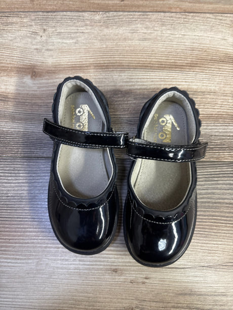 Top view of See Kai Run toddler Mary Jane shoes showcasing black patent finish, scalloped edge and Velcro strap on wood floor