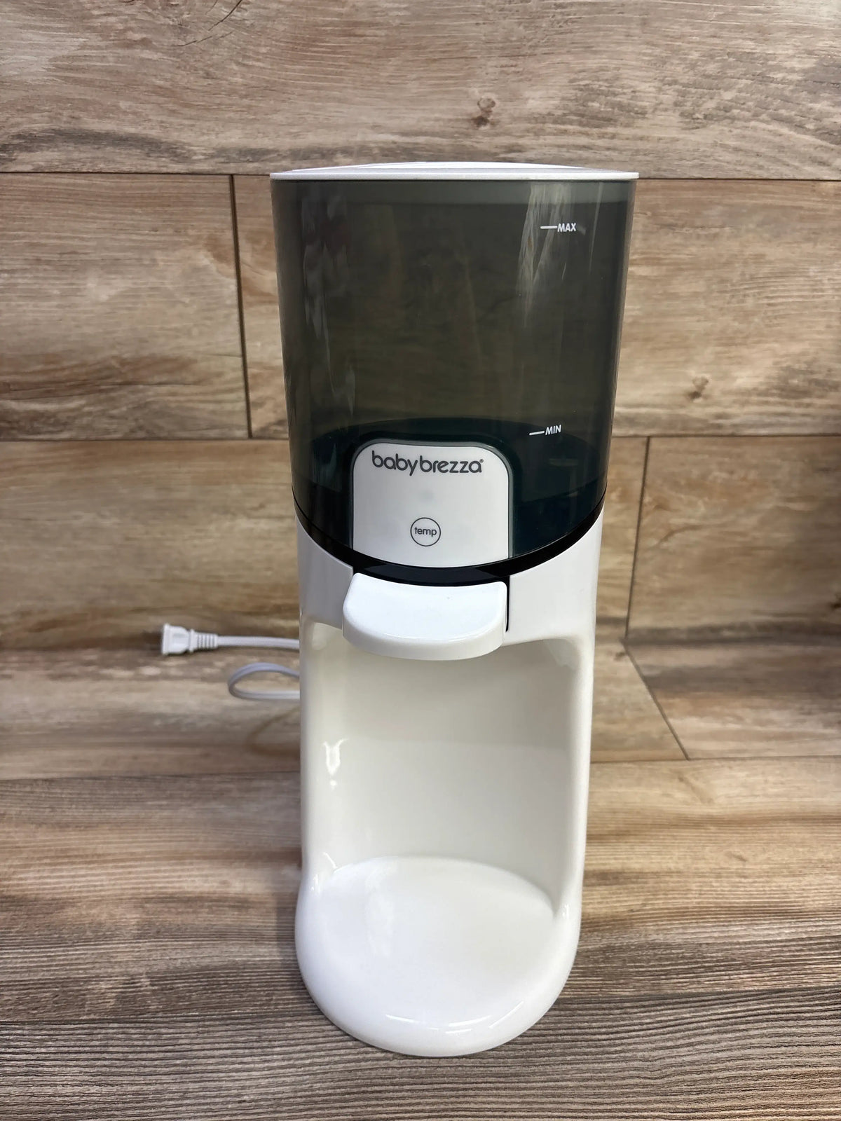 Front view of Baby Brezza Instant Bottle Warmer showing MAX and MIN markings and temperature button on wood grain