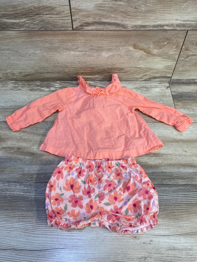 Flat lay of coral baby 2-piece: ruffled swiss-dot long-sleeve top and floral elastic shorts on wood background, 6M