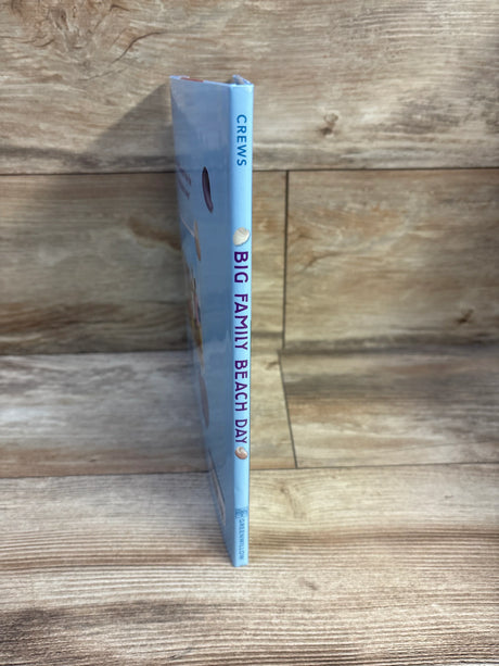 Side view of Big Family Beach Day hardcover showing blue spine with title, by Crews, and shell icons on wood background