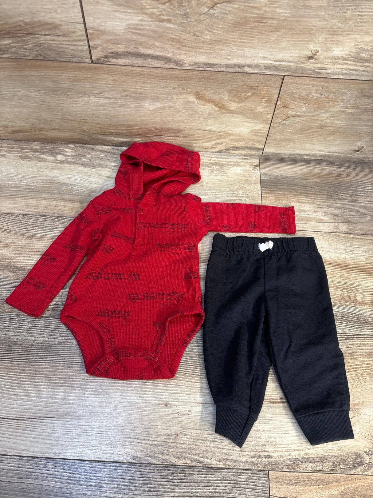 Flat lay of Carter 2pc Waffle Knit Hooded Bodysuit and Joggers Set Red sz 6m showcasing red hooded long sleeve bodysuit with black print and matching black joggers on wood plank floor