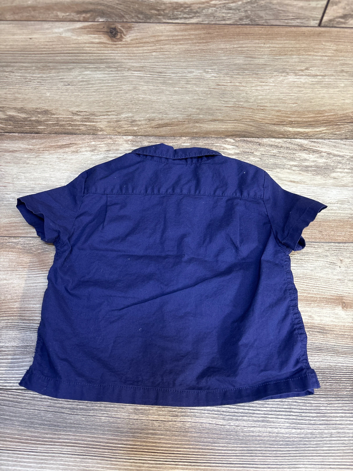 Back view of a short sleeve navy blue kids shirt on wood floor