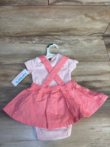Pink baby girl dress with attached skirt and cross straps, displayed on a hanger, wooden background