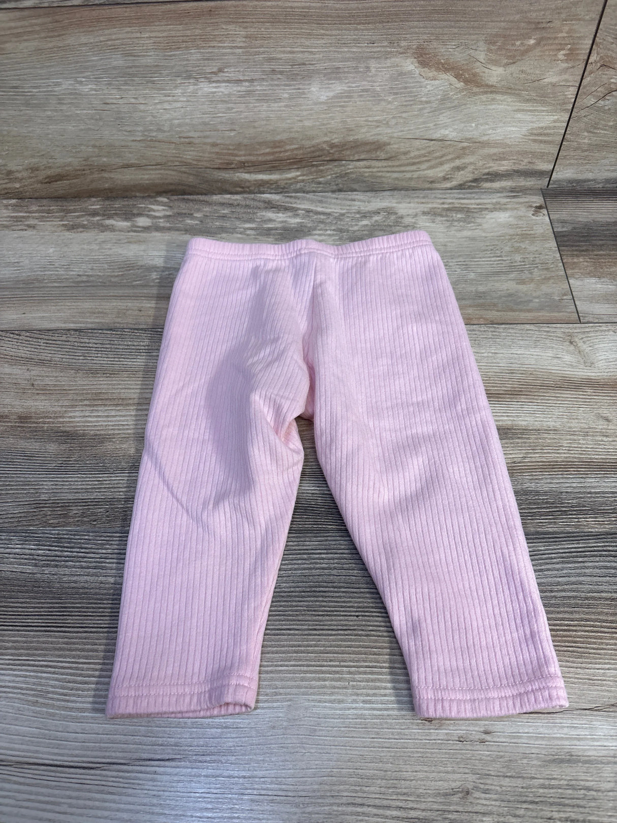 Flat lay of Carter's pink ribbed baby leggings, size 24 months, showing ribbed texture and elastic waistband on wood floor background