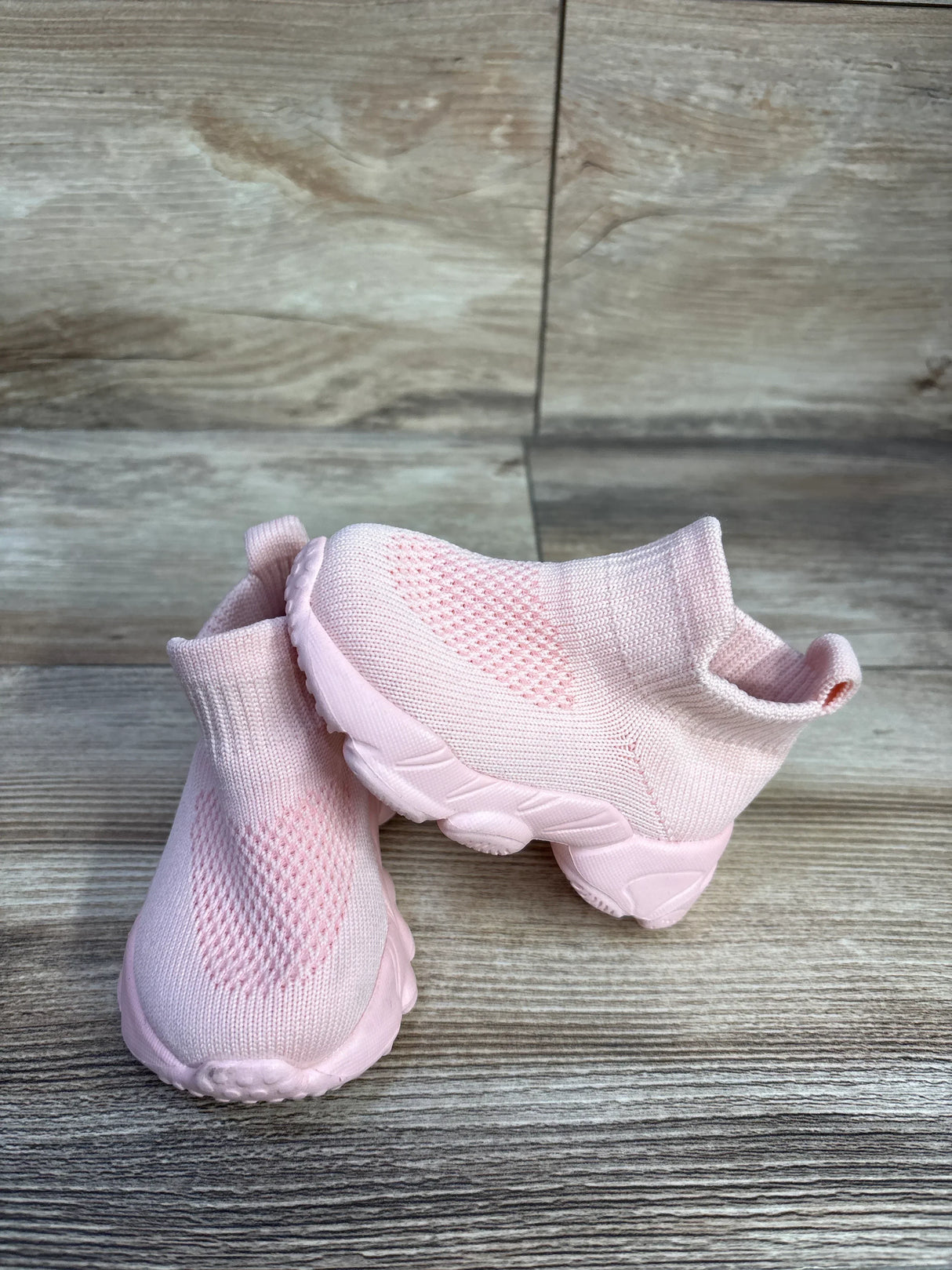 Angled view of pink high-top mesh sock shoes showing knit upper, ankle sock cuff and chunky sole on wood background