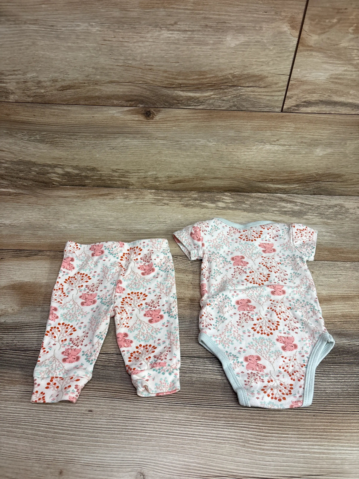 Top-down view of The Peanutshell ivory bodysuit and pant set with floral print and blue trim on a wood background