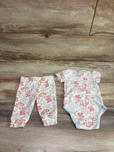 Top-down view of The Peanutshell ivory bodysuit and pant set with floral print and blue trim on a wood background