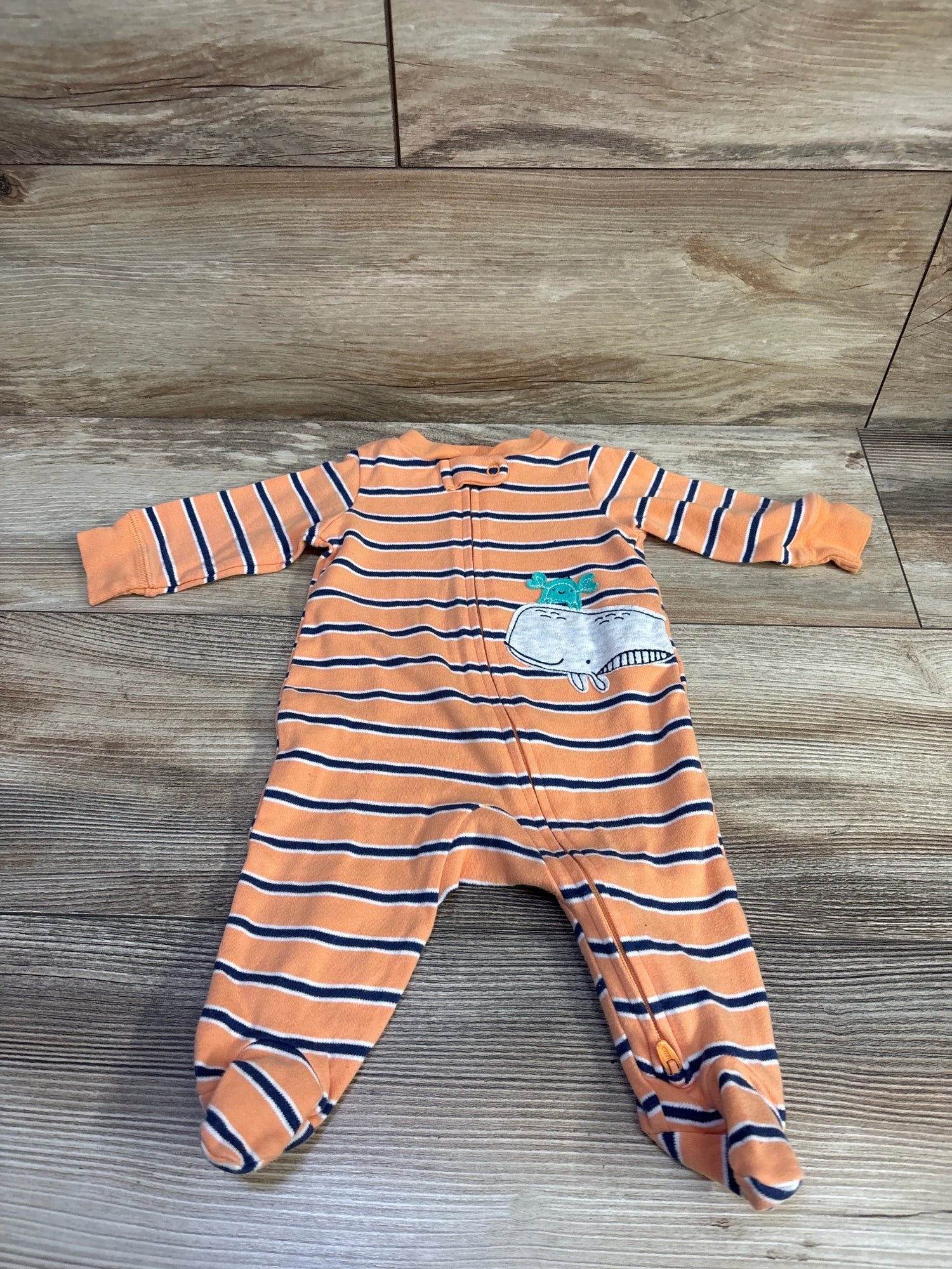 Front view of Carters orange striped footed sleeper in size 3 months showcasing a whale applique and front zipper on a wood-look floor