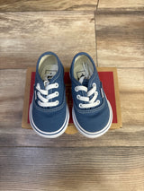 Top-down view of navy Vans Authentic low-top toddler sneakers showing white laces and rubber sole on a red box on wood floor