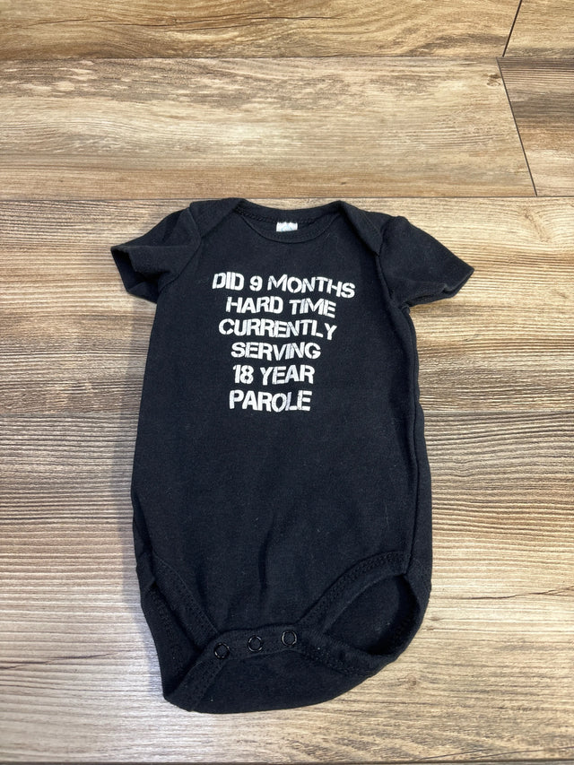 Flat lay of black newborn bodysuit showing white text Did 9 months hard time currently serving 18 year parole on wood background