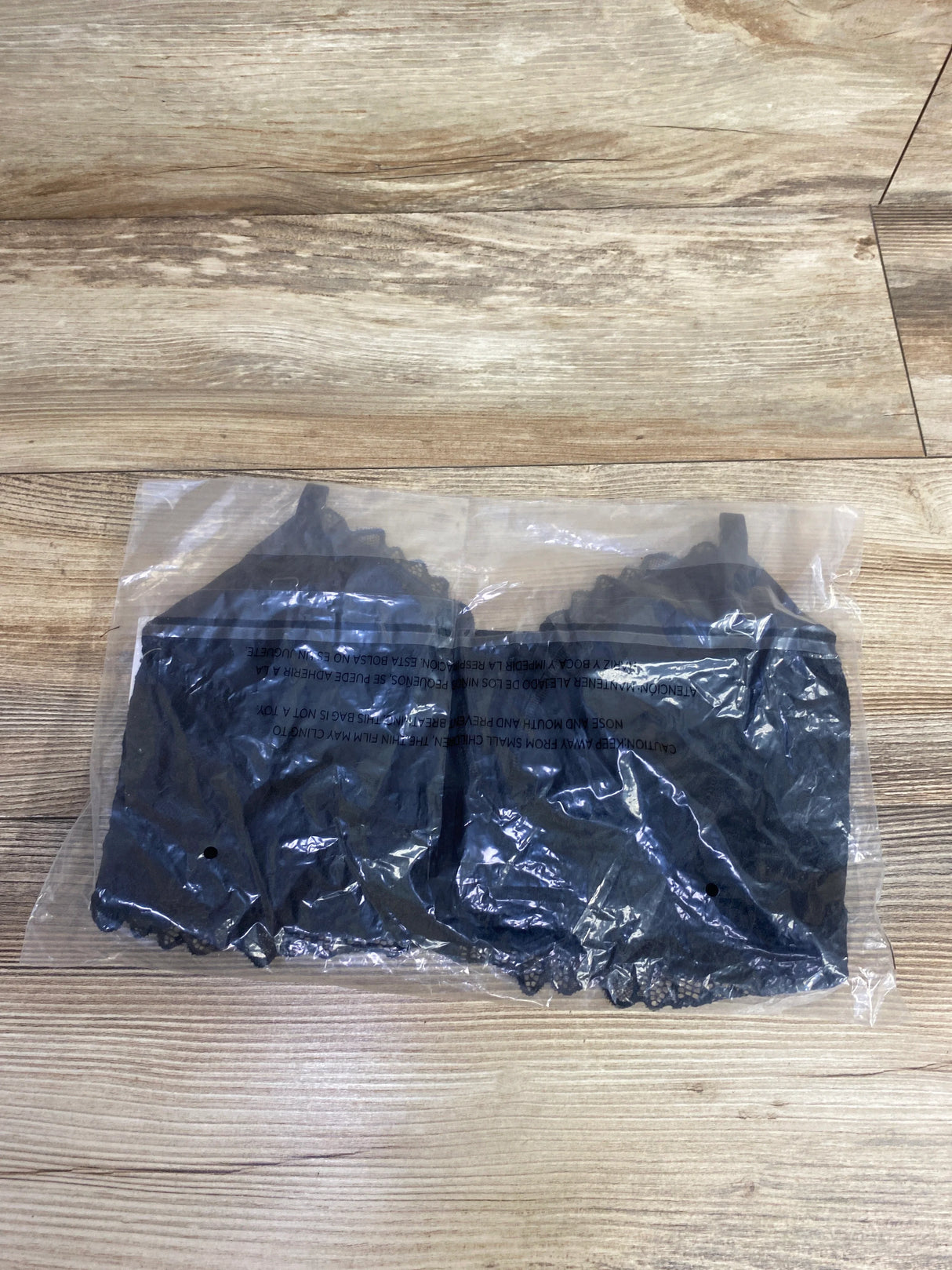 Black lace bralette packaged in clear plastic on wooden floor, children's resale store product