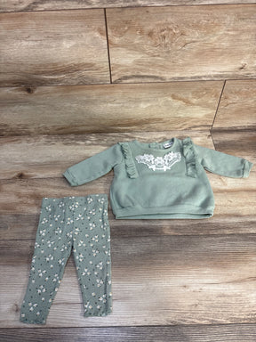 Green toddler outfit with long sleeve ruffle sweatshirt and floral patterned leggings on wooden floor