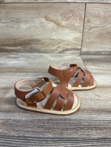 Three-quarter view of brown soft-sole baby sandals size 1C showing crisscross straps and ankle Velcro on wood background
