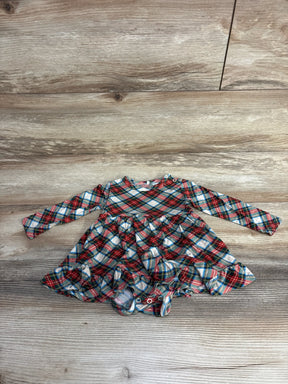 Plaid baby dress with ruffled skirt, long sleeves, and snap closures on wood floor