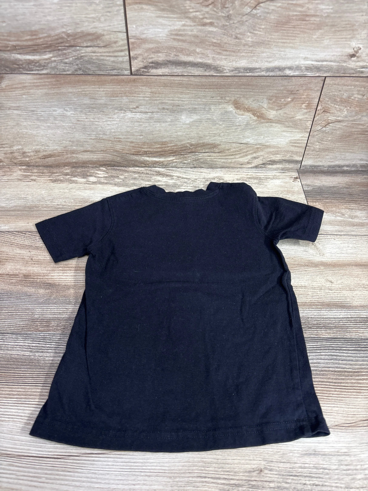 Back view of French Toast black toddler shirt showcasing short sleeves, size 4/5T, flat lay on wood floor