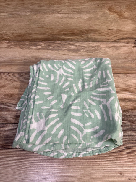 Top view of folded Momcozy bamboo swaddle blanket showing green fabric with white abstract leaf pattern on wood background