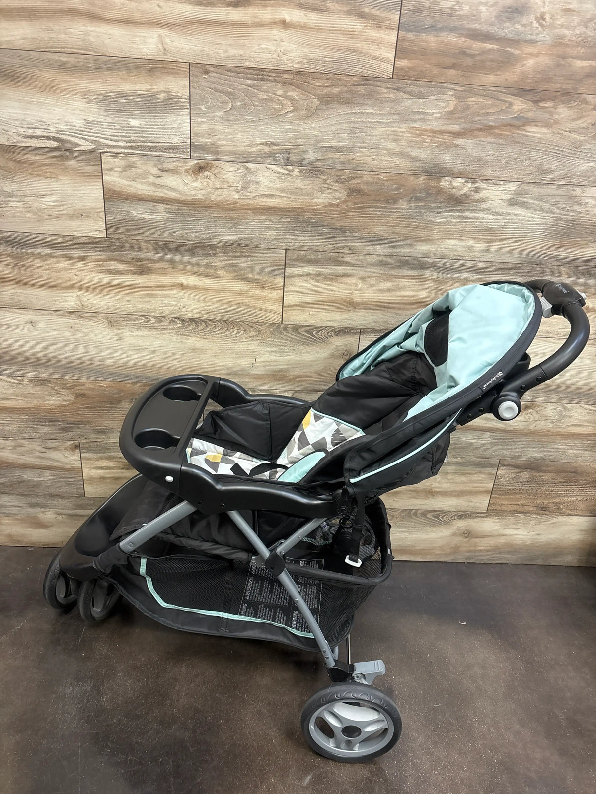 Angled view of Baby Trend EZ Ride Stroller in Doodle Dots showcasing aqua and black seating, front tray, and storage basket