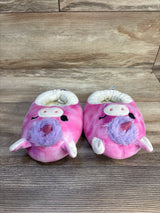 Pink plush unicorn baby slippers with purple mane on wood floor