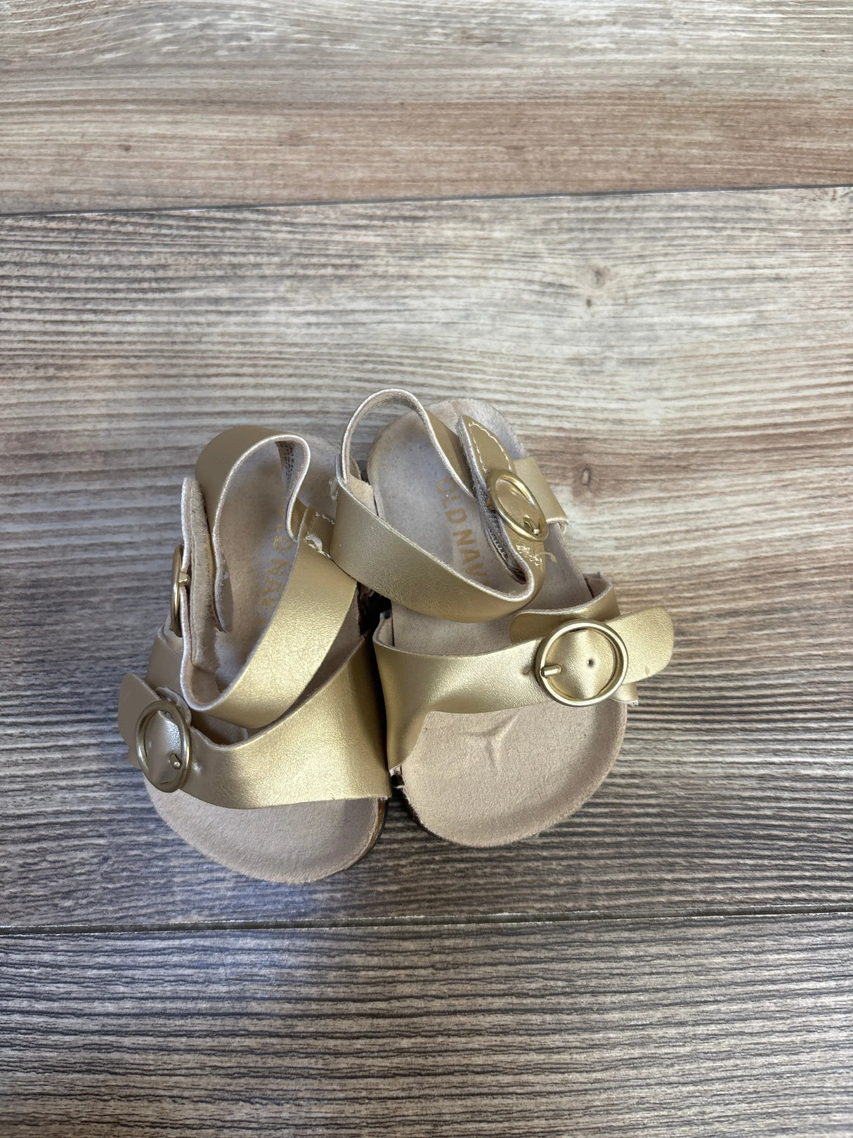 Gold toddler sandals with buckle straps on wooden background, gently used kids footwear
