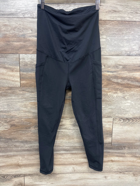 Front view of black maternity crossover panel leggings showcasing side pockets on a wood-look floor