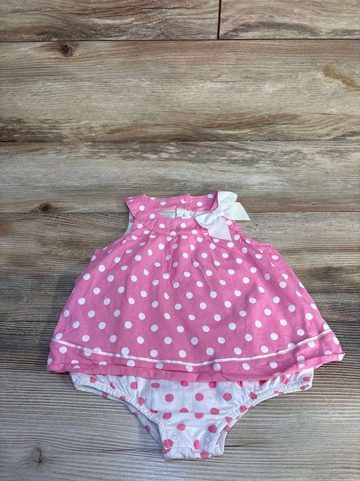 Flat lay of pink polka-dot bodysuit dress with white shoulder bow and matching bloomer on wood background