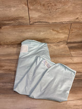 Top-down view of The Ollie World newborn swaddle in light blue showing Velcro closure and care label on a wood floor