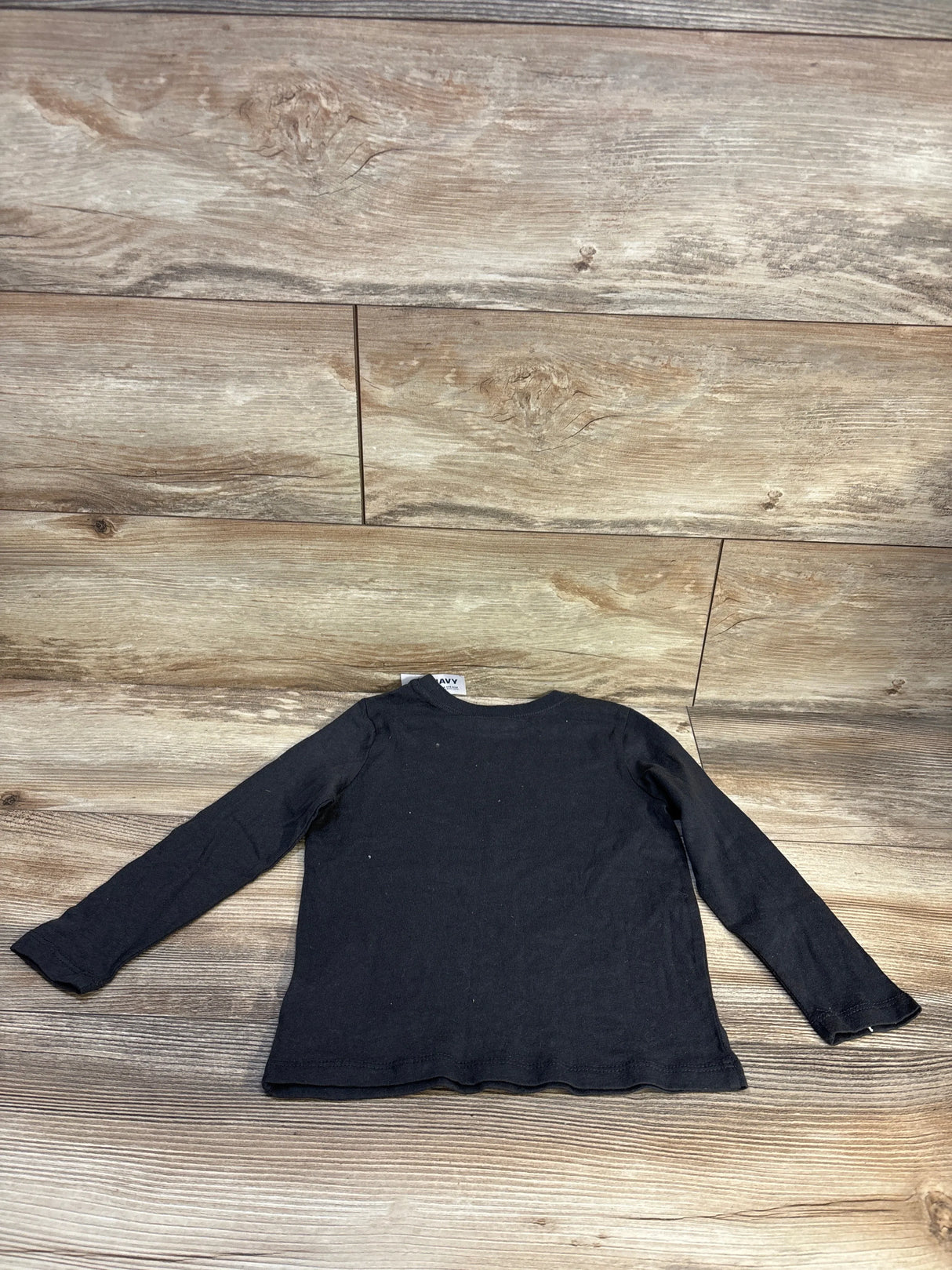 Black long sleeve kids shirt laid flat on wooden surface, children's clothing resale