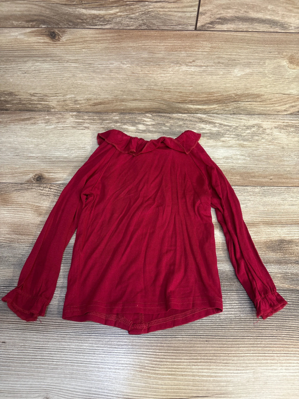 Red long sleeve girls shirt with ruffle collar and cuffs on wood background
