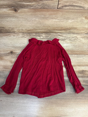 Red long sleeve girls shirt with ruffle collar and cuffs on wood background