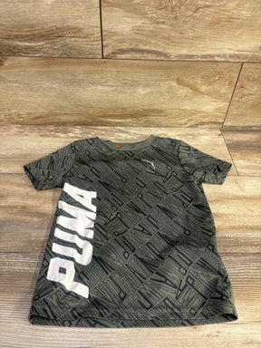 Front view of a green Puma shirt in size 4T showcasing a geometric pattern and white Puma logo on a wood floor