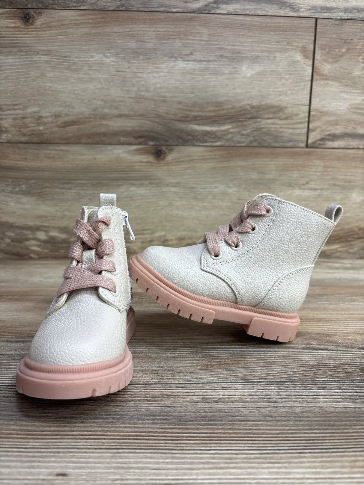 Pair of white toddler boots with pink soles and laces on wooden floor background
