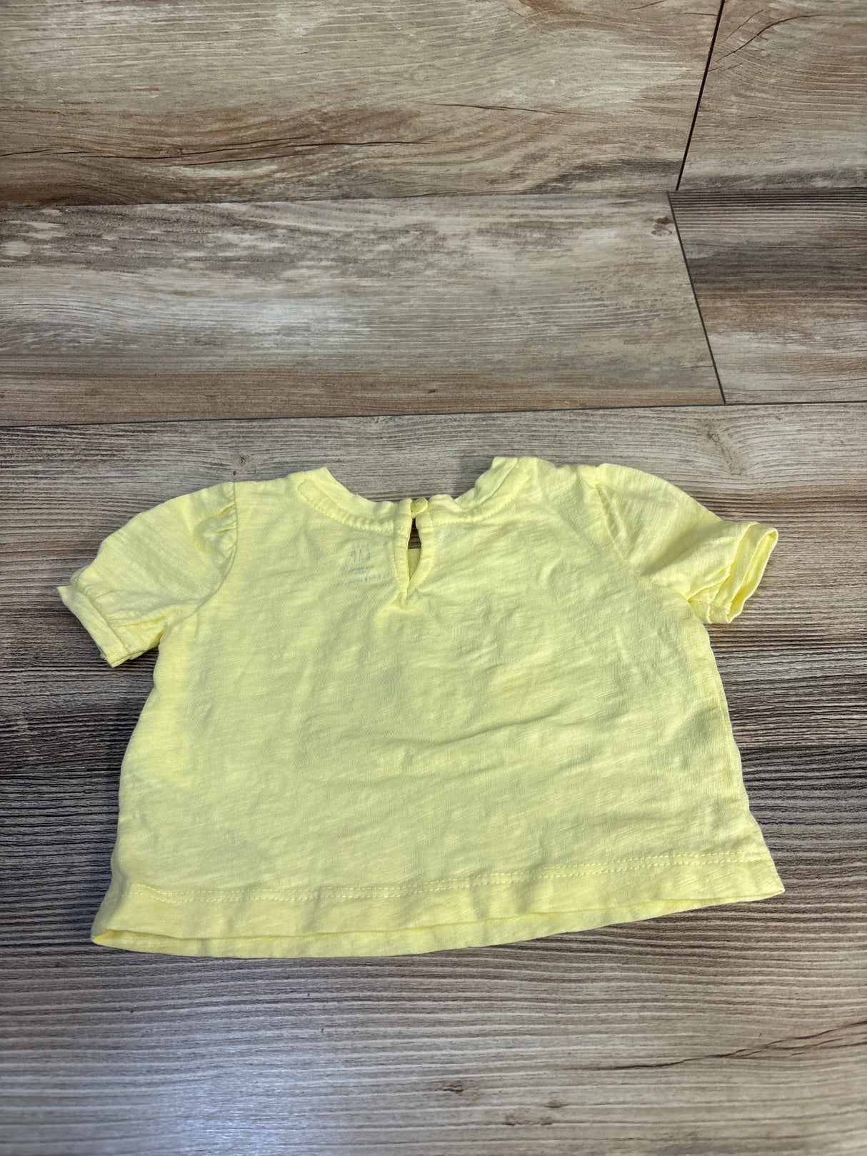 Yellow baby short sleeve shirt with button neck, laid on wood floor