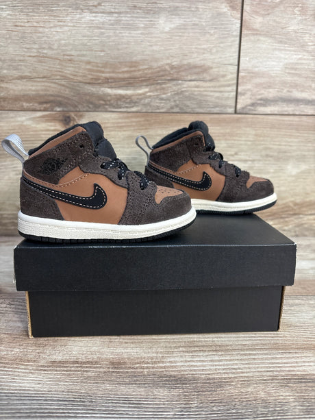 Brown and black toddler high top sneakers with white soles on a shoe box, wood background