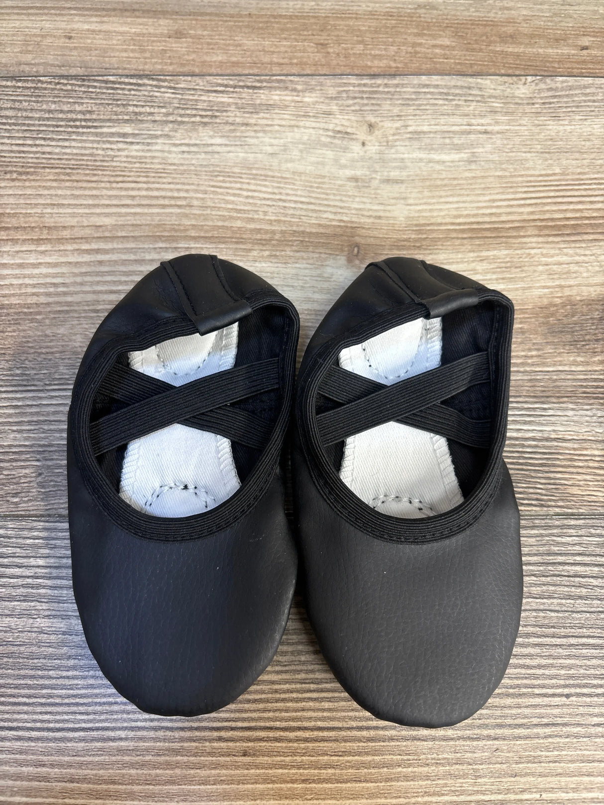 Black toddler ballet flats with elastic straps on wood background