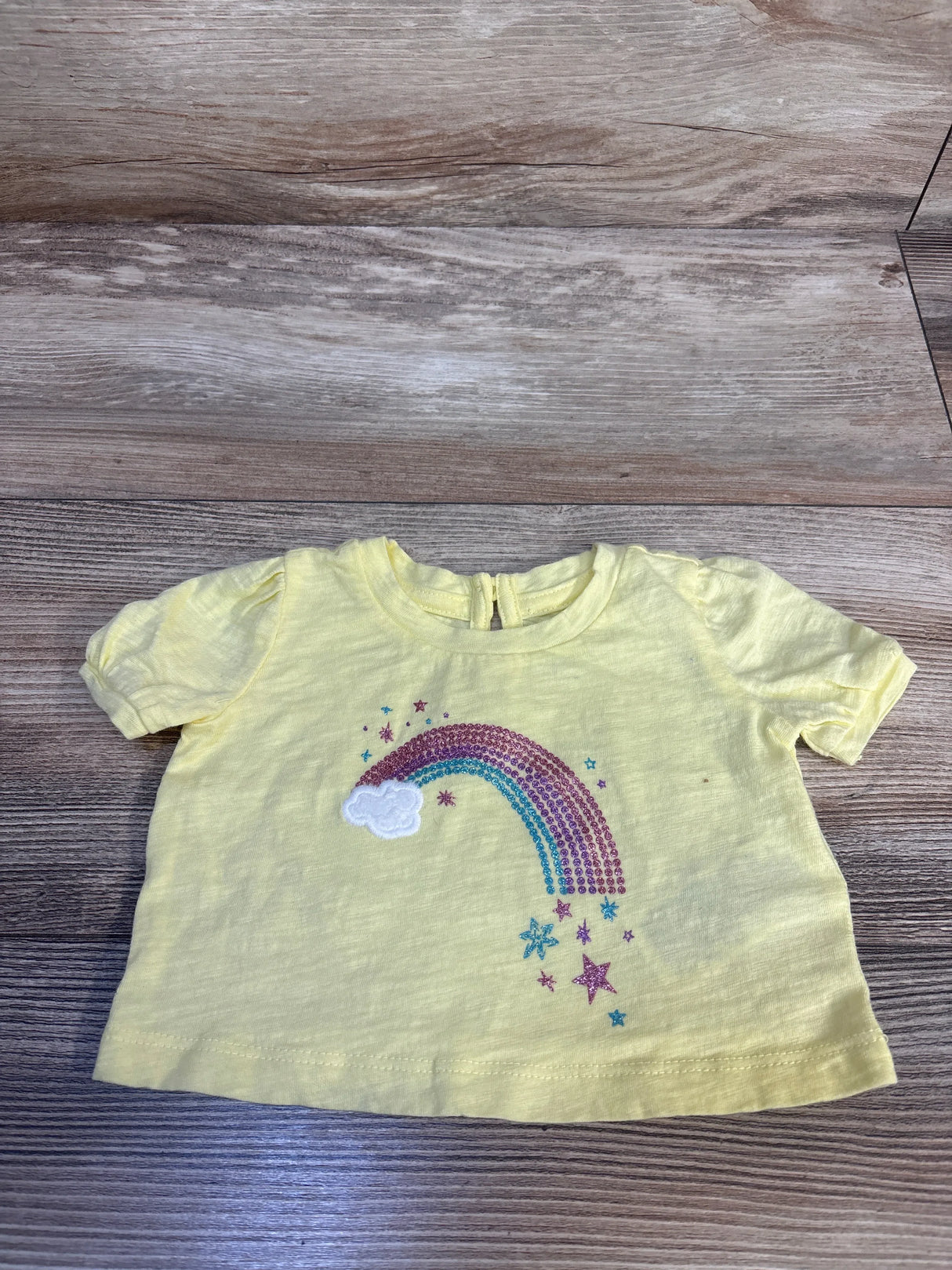 Yellow toddler tee with glitter rainbow, cloud, and stars design on wood floor
