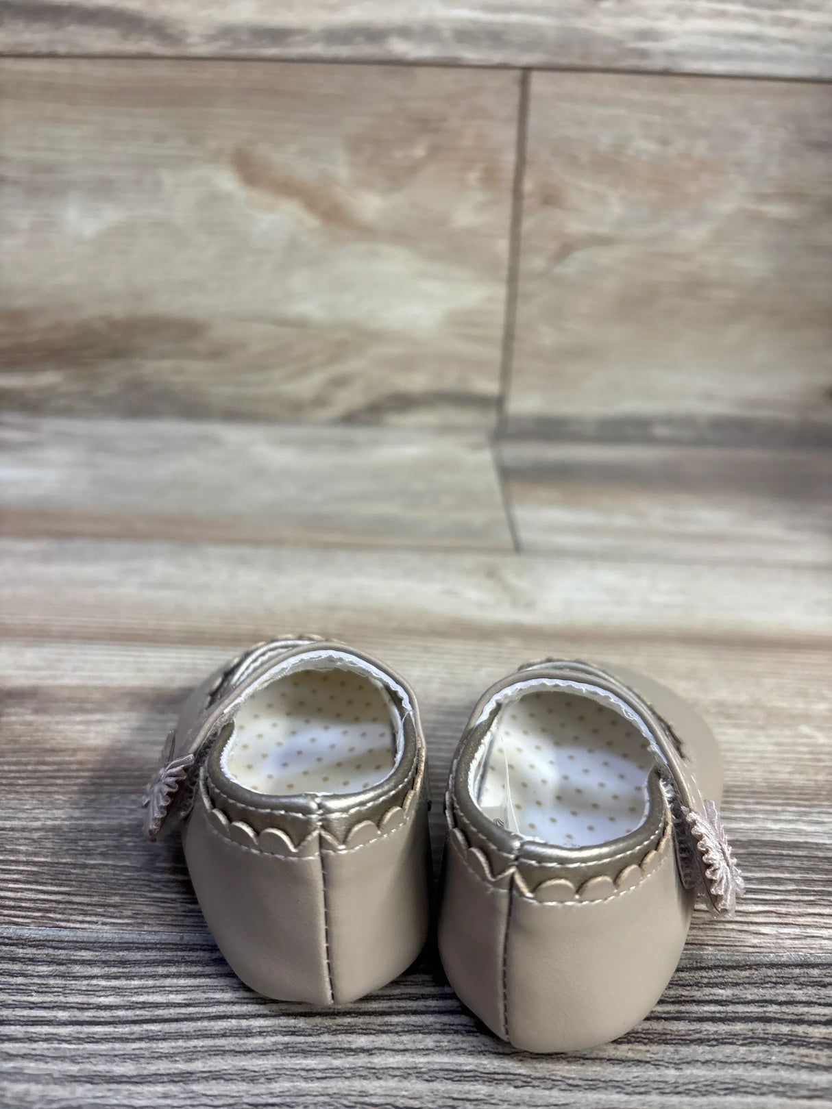 Rear view of tan Mayoral Mary Jane baby shoes showcasing scalloped trim, side flower straps and polka dot lining on wood floor